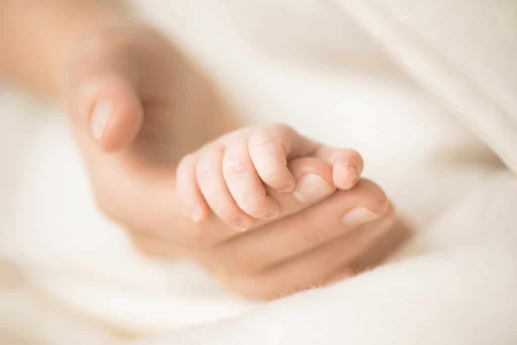 Female hand holding her newborn baby's hand. Mom with her child. Maternity, family, birth
